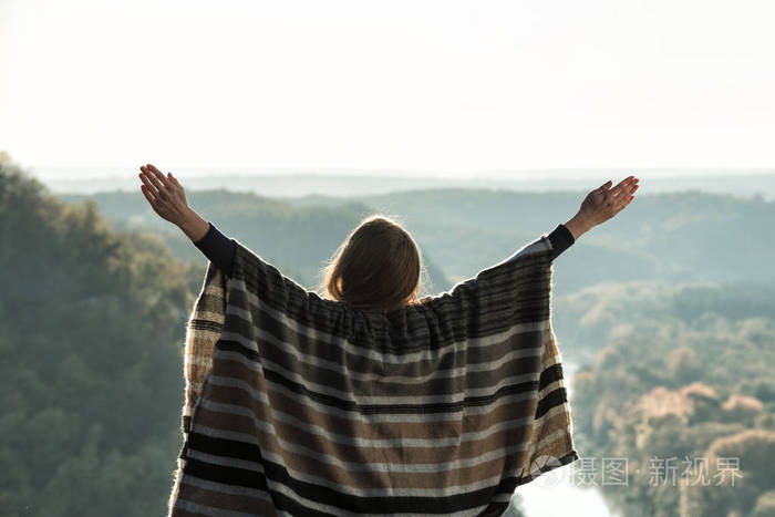 在山上享受阳光的年轻女子举起双手后视图