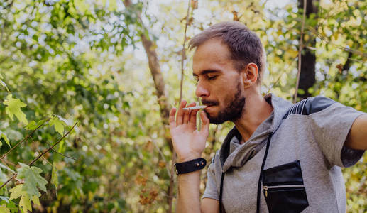 年轻人抽烟并产生烟雾,户外潮人肖像.成熟的有胡子的时髦人士.照片