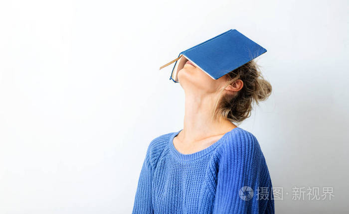 年轻女子用书遮住脸的横向图像一位穿着蓝色针织毛衣的漂亮女子把脸藏