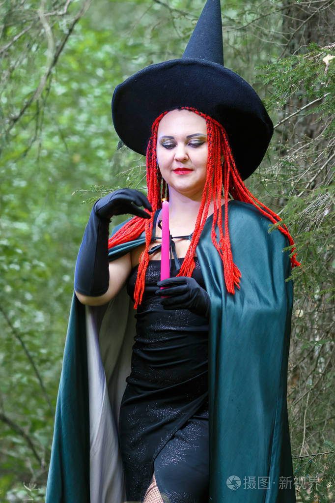 森林里一位红发头戴尖顶帽披着黑色斗篷的女巫正在用蜡烛施魔法