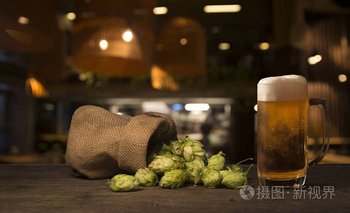 啤酒酿造原料放进袋子里，小麦穗放在破旧的木制桌子上。啤酒厂概念。啤酒花球果和小麦特写。一袋啤酒花和一捆小麦放在古老的背景上。