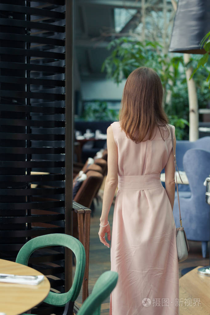 从餐厅里一个穿着粉红色长裙留着一头深色长发的苗条女孩的后背望去