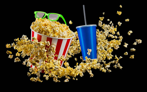 纸条桶里放着爆米花,一杯饮料和一杯隔离的黑色玻璃杯照片