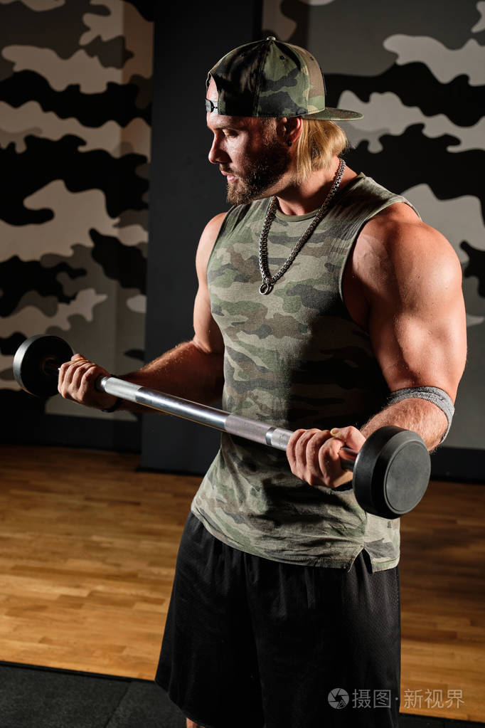 一个肌肉发达的男人穿着t恤戴着棒球帽弯着胳膊垂直地握着杠铃