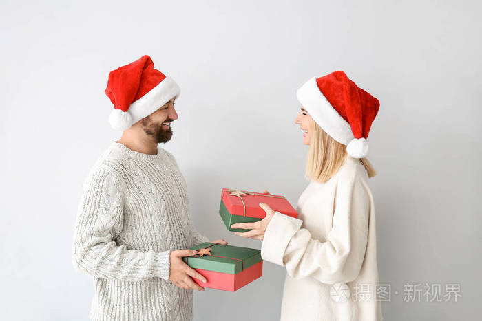 一对幸福的情侣在浅色背景下互相赠送圣诞礼物