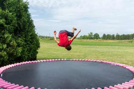 一个穿着红衬衫的小男孩在蹦床上翻筋斗做体操动作.概念.照片