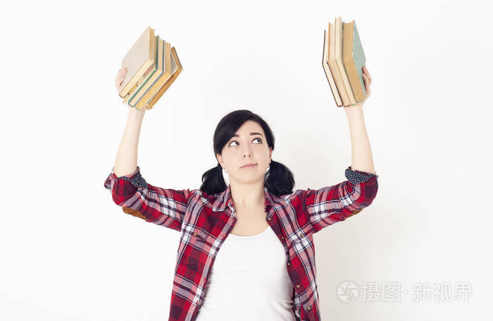 一个穿红色格子衬衫的女学生双手捧着一摞书准备进入大学课程或考试