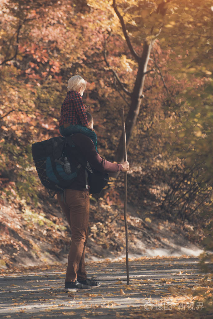 父亲背着儿子在秋天的公园里跋涉阳光明媚的一天后视图