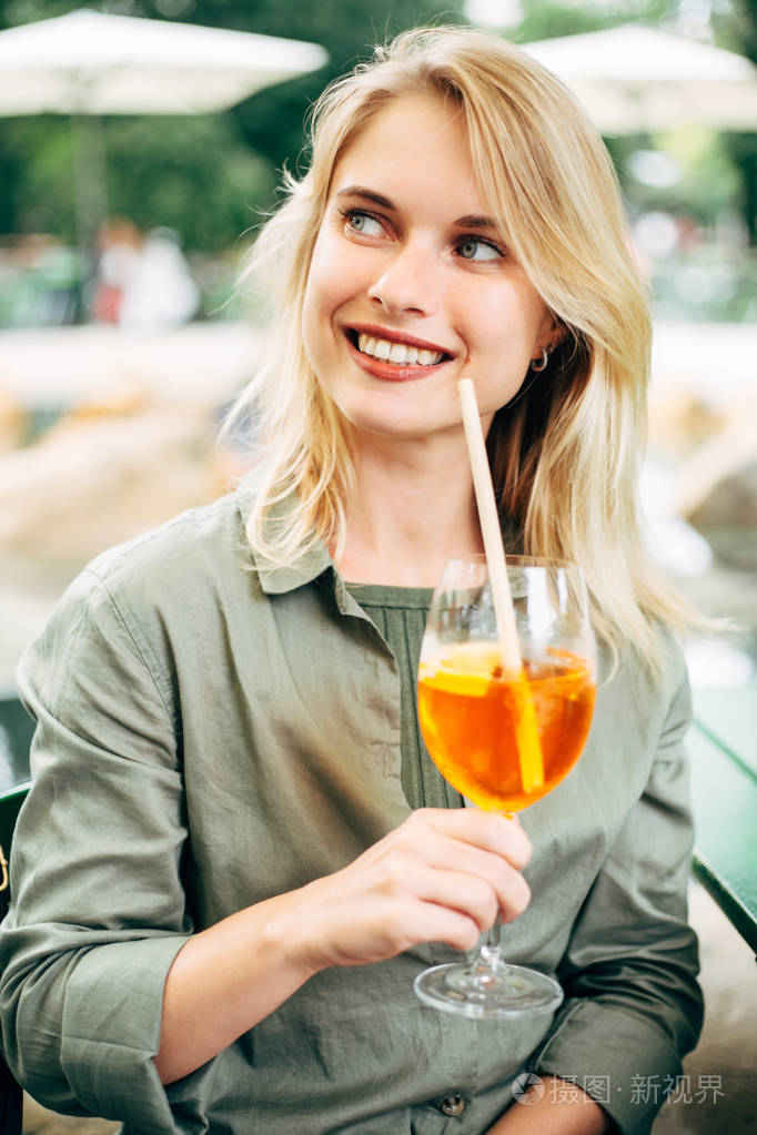 照片中是一位快乐的金发女子手里拿着鸡尾酒