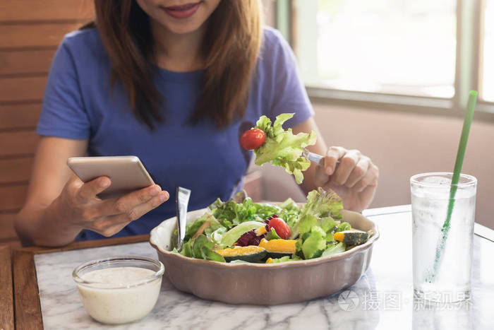年轻女子在餐厅用智能手机吃饭