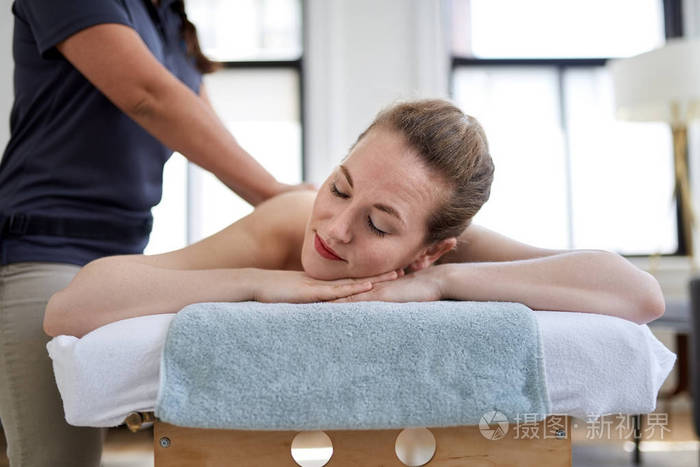 在一间明亮的医务室里一位中国女按摩师正在按摩桌上为一位漂亮的金发