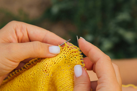 高织高密夏天,一个金发碧眼的小女孩在花园里织一件黄色的毛衣.