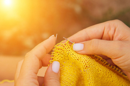夏天,一个金发碧眼的小女孩在花园里织一件黄色的毛衣.