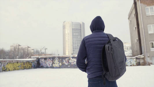 一个穿着深蓝色夹克和背包的男人站在城市街道和涂鸦墙上.行动.