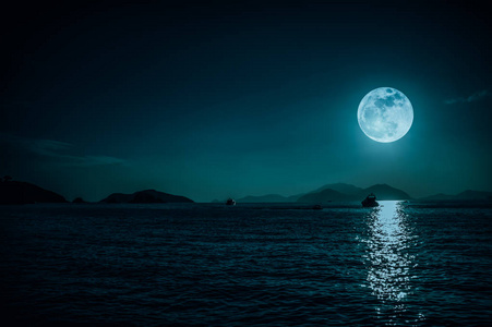 夜晚和满月时平静海水中小船的风景.摄影图