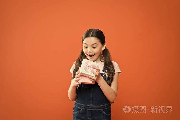 可爱的小孩打开礼物盒,橙色背景上有一张惊喜的脸.