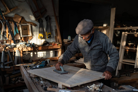 很老的木匠师傅在家里的作坊里打磨木头,工作很努力照片