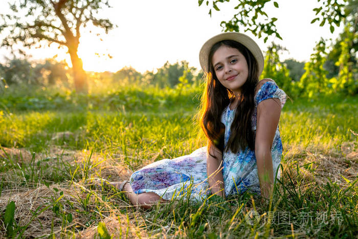 快乐美丽的女孩深色头发穿着印有花朵图案的连衣裙戴着白色帽子坐在