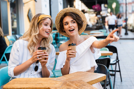 快乐的年轻积极乐观的女孩朋友们坐在户外的咖啡馆里喝咖啡聊天.照片