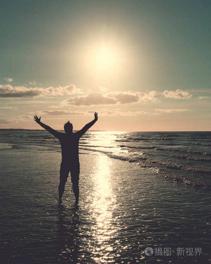 一个男人张开双臂在海边晒太阳面对夕阳的倒影夏季和旅游概念复古外观