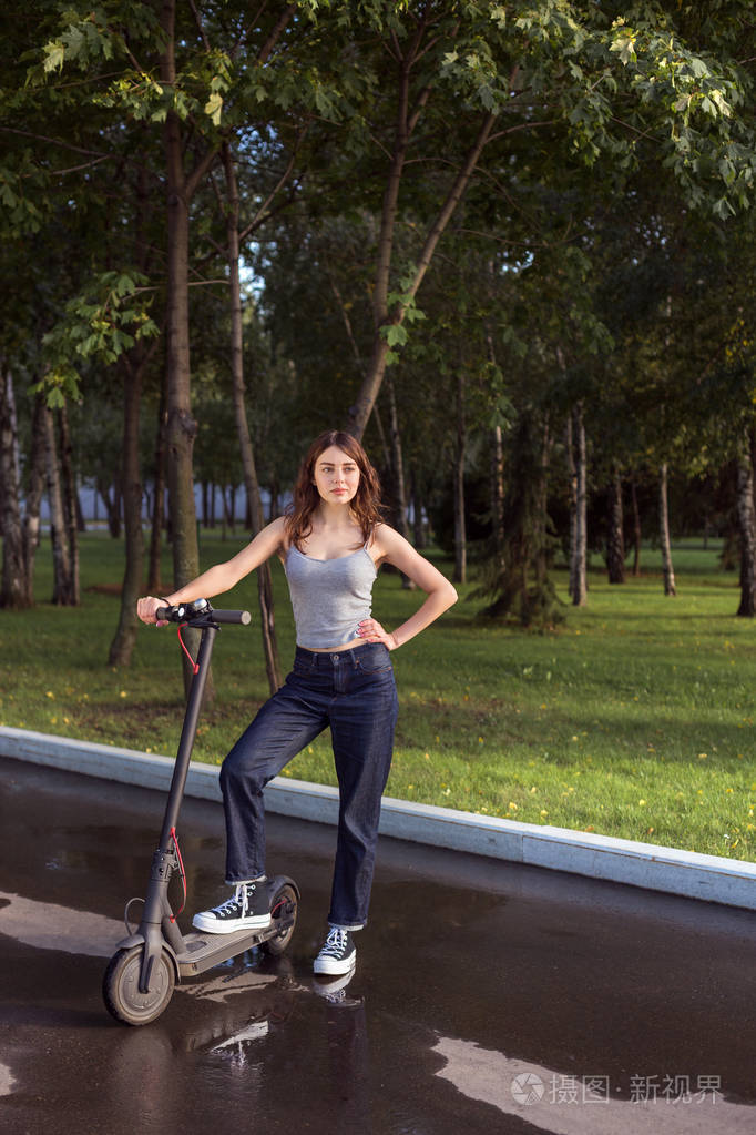 阳光明媚的公园人行道上黑发女孩骑着环保电动踢板车