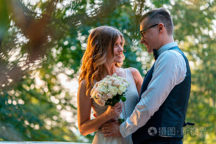 新婚夫妇紧紧地站在一起微笑着拥抱着日落的公园背景模糊