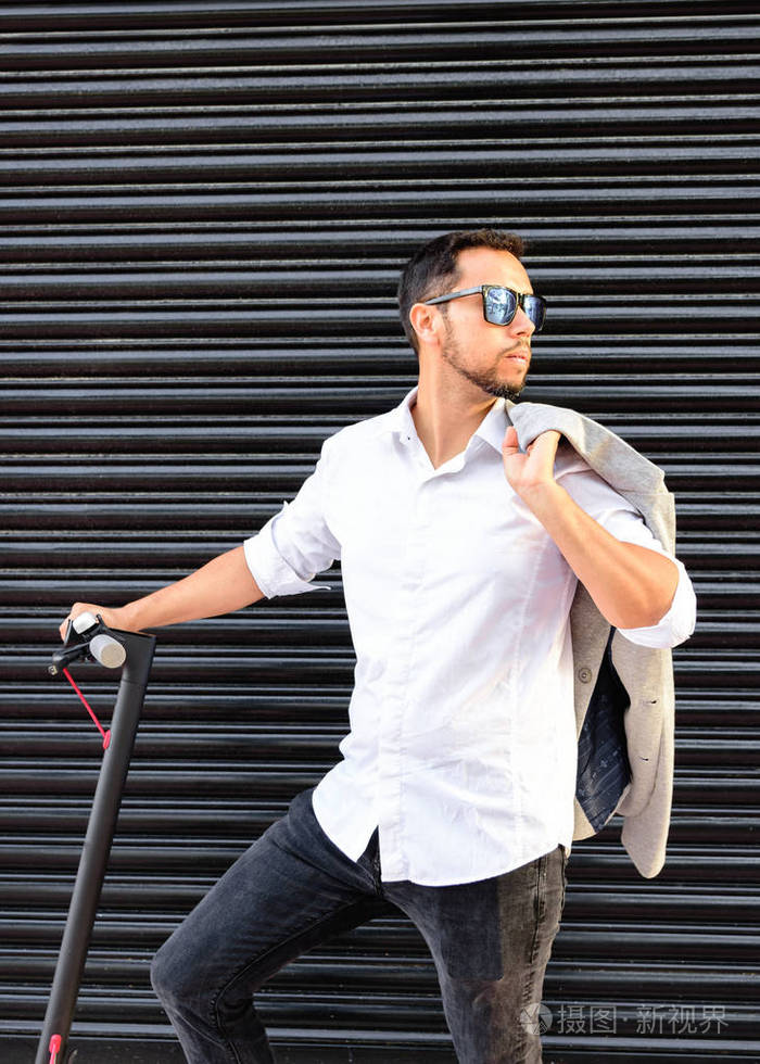 着墨镜,穿着得体,骑着电动车在街上用手机聊天,背景是一个黑色的盲人