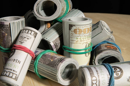 一堆美元钱在一个黑色的背景下卷成一个管子照片