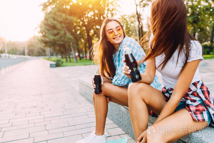 两个时髦的女朋友坐在公园里喝一杯