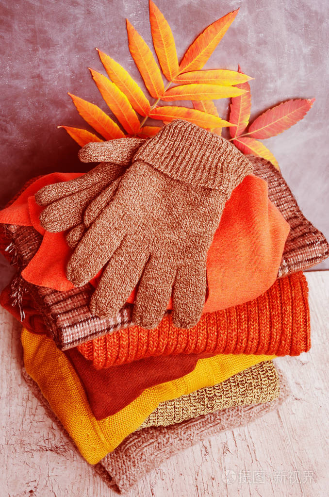 一摞叠好的保暖针织女式毛衣围巾手套暖色系秋叶鲜艳特写