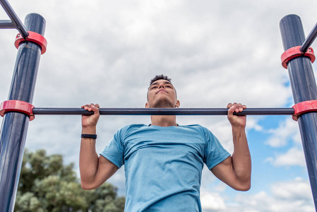 男运动员把自己拉上单杠,训练强壮有力,在夏日的城市里,下午空气清新.