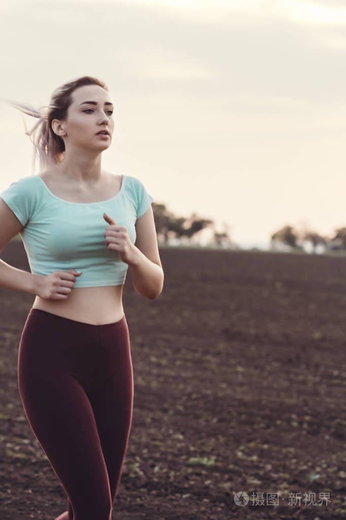 美丽的年轻女子穿着运动服在赛场上奔跑女孩在阴天从事户外运动概念