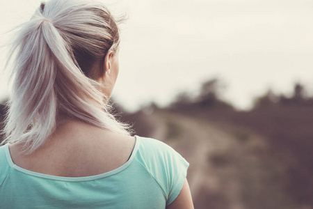 女性后脑勺在田径场慢跑的背景上,女孩用马尾辫进行体育运动照片