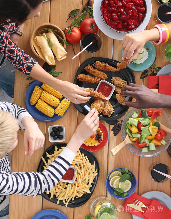 坐在木桌旁吃饭的人群的俯视图餐桌上的食物人们吃快餐