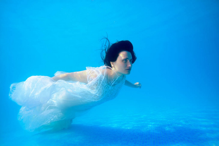 阳光明媚的日子里,一个穿着白色婚纱的可爱女孩漂浮在水底附近的水下.