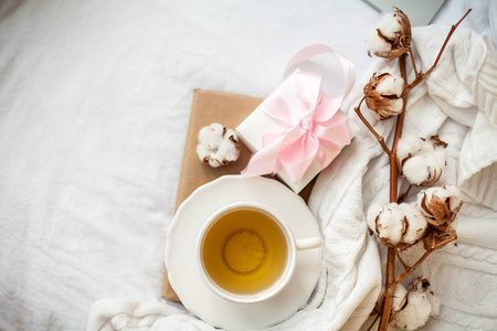白色马克杯,配有茶,棉布,格子花呢,书和白色礼品盒,床上有粉色丝带.