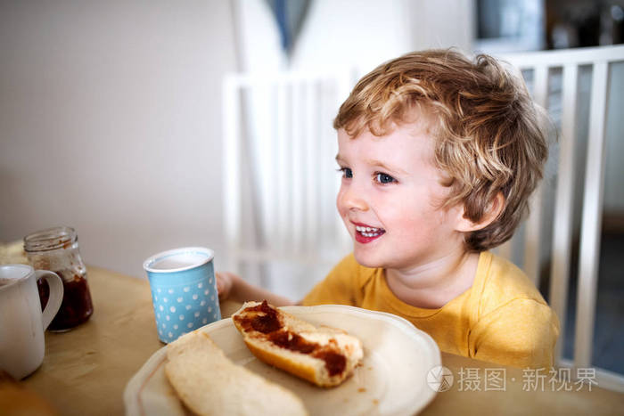 一个蹒跚学步的男孩在家里吃饭的正视图。
