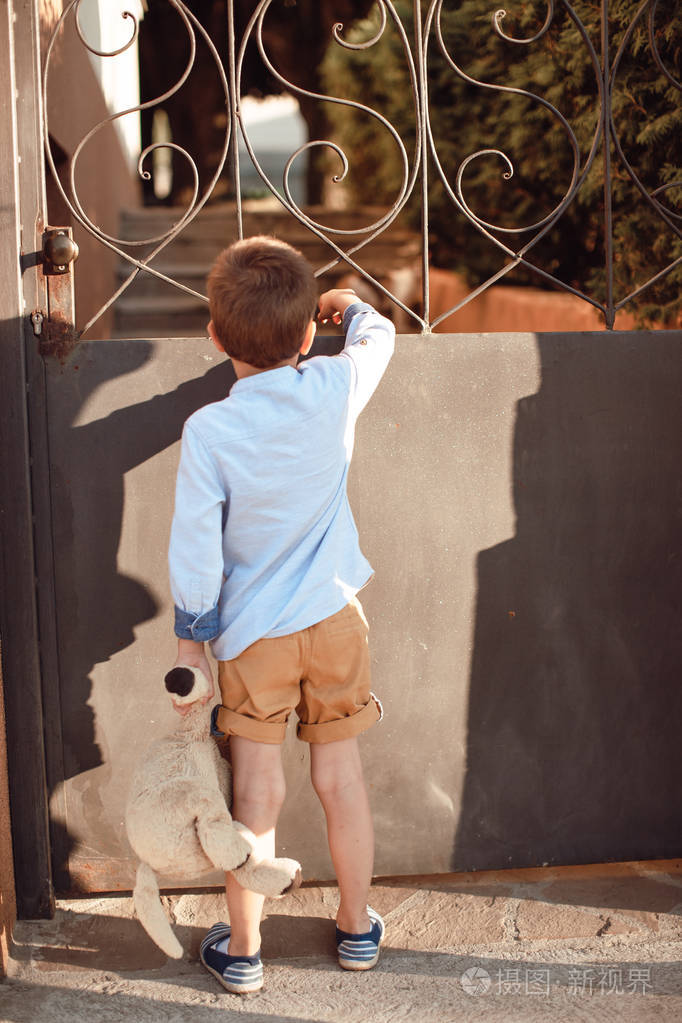 可爱的小男孩抱着他的泰迪熊站在门口
