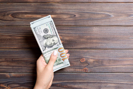 空间工资一只手拿着一捆一百美元钞票的木头背景.