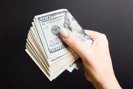 女人的手紧紧握着一捆钱.彩色背景下的100美元的俯视图.投资理念照片