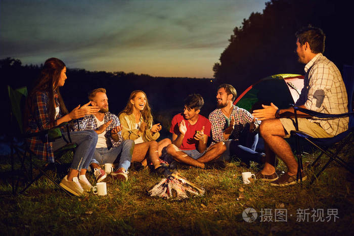 秋天的夏天，晚上一群人坐在帐篷旁的篝火旁。