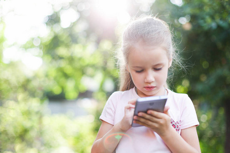 孩子在看设备的屏幕.小女孩正在外面的绿色公园或花园里玩电子产品.