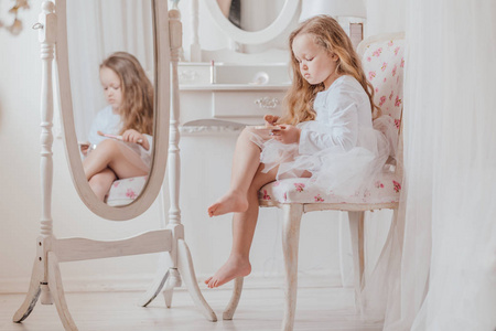小孩桌子上拿玩具一个拿着化妆刷的小女孩独自坐在白色房间里大镜子
