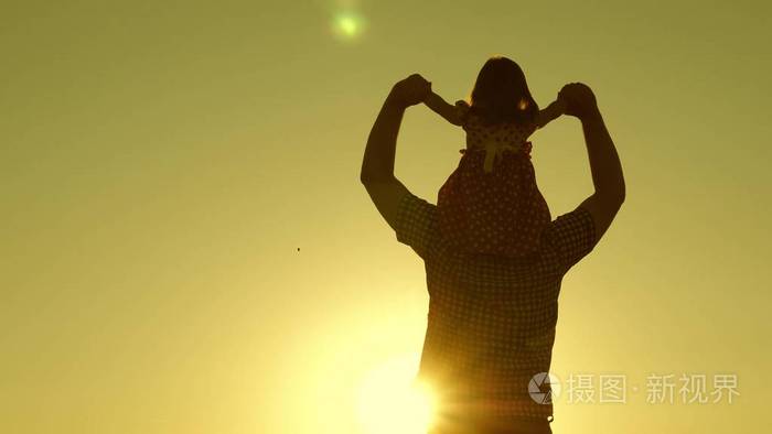 夕阳下爸爸肩上背着心爱的孩子在田野里走来走去小女儿骑着爸爸的肩膀