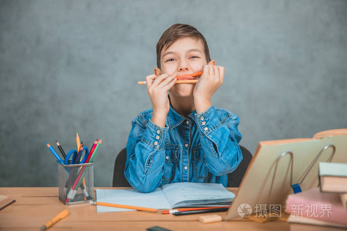 在学习过程中，一个快乐的小男孩在玩铅笔。书桌上有一摞书和几只山核桃。