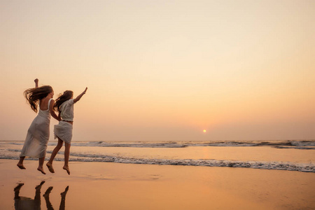 夕阳下,幸福的母亲和小女儿在海边玩得开心.