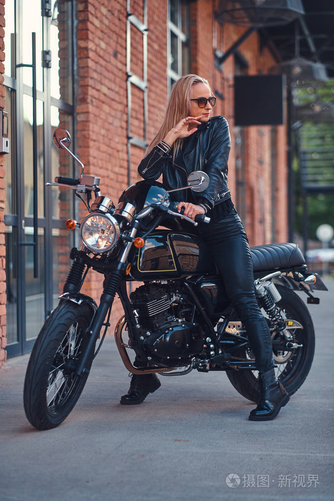 英俊的女摩托车手拿着摩托车摆姿势给摄影师拍照