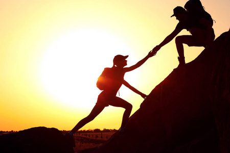 爬山剪影男人和女人在夕阳下互相帮助爬山的剪影照片