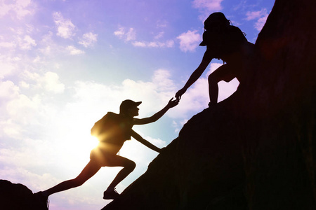 男人和女人在夕阳下互相帮助爬山的剪影