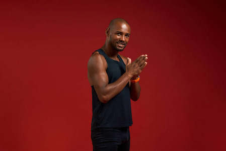 站在红色背景下,年轻的非裔美国人双手合十,微笑着看着相机照片